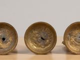 three antique brass candlesticks on a wooden table with a white wall in the background