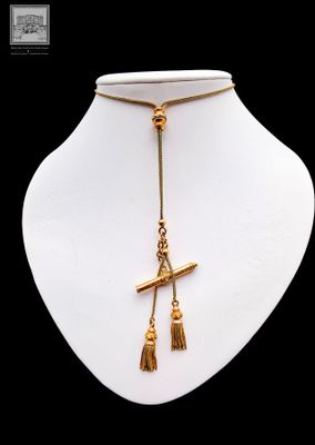 a gold necklace with a cross and tassel on a mannequin