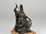 a bronze statue of a woman sitting on a rock holding a sword