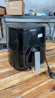 une friteuse à air chaud Philips posée sur une table en bois, avec une boîte de nourriture en arrière-plan