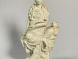une statue blanche représentant une femme assise sur un rocher