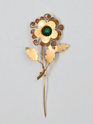 une image représentant une broche en forme de fleur dorée et verte sur fond blanc