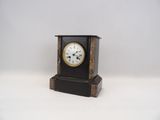 une petite horloge noire avec un cadran blanc sur fond blanc