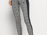 a woman in black and white patterned leggings stands against a white wall