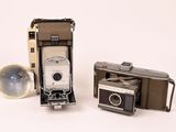 two old cameras sitting next to each other on a white surface