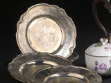 trois assiettes en argent et une théière en argent posées sur une table noire