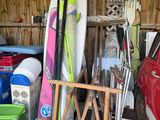 Plusieurs planches de surf sont empilées dans un garage, à côté d'une voiture rouge