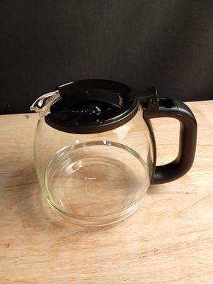 une théière en verre avec un couvercle noir posée sur une table en bois