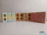 trois boîtes contenant des ombres à paupières de différentes couleurs, posées sur une surface blanche