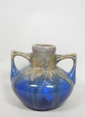 un vase bleu à deux anses posé sur une surface blanche