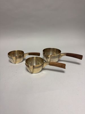 three brass measuring cups with wooden handles on a white surface