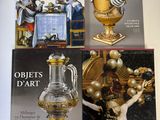 trois livres posés sur une table sur laquelle se trouve un vase doré