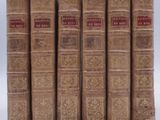 six old books are lined up in a row on a white surface
