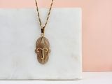 un collier plaqué or avec un pendentif en forme de visage posé sur un bloc de marbre