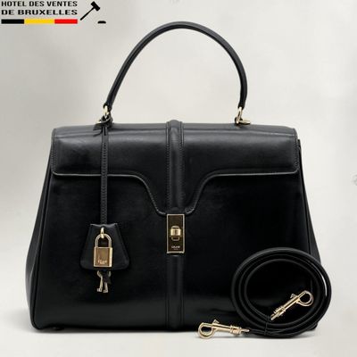 le sac à main en cuir noir se trouve à côté d'un cadenas doré sur fond blanc