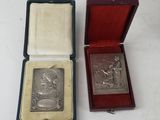 two small silver plaques in a red box on a white surface