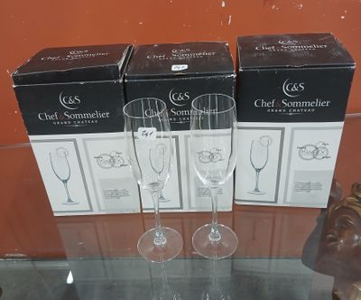 trois verres à vin posés sur une table en verre, à côté de cartons de vin