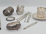 de nombreux objets en argent posés sur une surface blanche, notamment une tasse à thé, une cuillère et d'autres objets