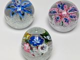 trois presse-papiers en verre ornés de fleurs, posés sur une surface blanche