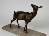 statue en bronze représentant un cerf, posée sur un socle en marbre, sur fond blanc
