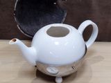 a small white teapot sitting on a table next to a coin