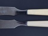 two cheese knives on a black surface with a knife in front of them