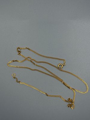 un gros plan d'un collier en or avec une chaîne, posé sur une surface grise