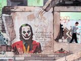 painting of a man walking past a wall with a picture of a clown on it