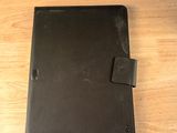 un étui en cuir noir pour iPad posé sur une table en bois à côté d'une chaise noire
