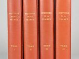 quatre livres rouges ornés de lettres dorées, posés sur une table