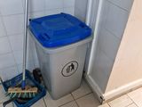 a trash can and a broom in the corner of a bathroom