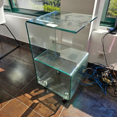 une table en verre surmontée d'une étagère en verre, placée devant une fenêtre