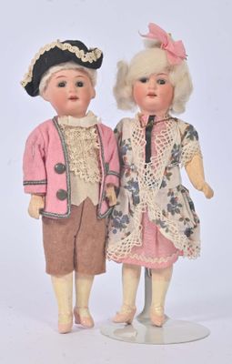 two dolls standing next to each other on a white surface
