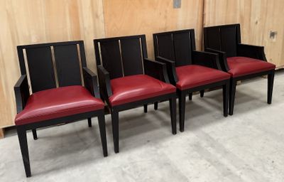 quatre chaises alignées, avec des sièges en cuir rouge, devant un mur en bois