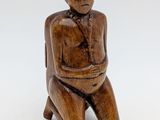 an old wooden figurine of a man sitting on a stool
