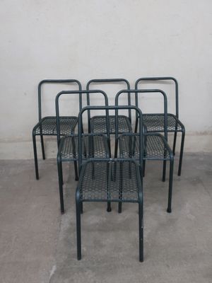 four metal chairs are lined up against a wall in a parking lot