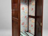 an antique wooden armoire with floral wallpaper and a mirror