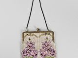 a white purse with purple flowers hanging on a chain
