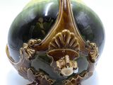 a green and gold vase sitting on a white surface