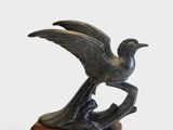 sculpture en bronze représentant un oiseau, posée sur un socle en bois, sur fond blanc