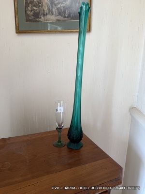 a green glass vase sitting on a wooden table next to a painting