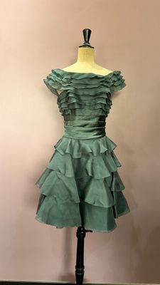 robe verte à volants posée sur un mannequin devant un mur rose