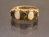 yellow gold ring with green and white stones on a black surface