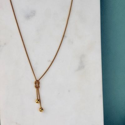 un collier en or orné d'une clochette, posé sur une dalle de marbre