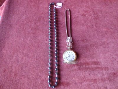 une montre de poche en argent et un collier de perles posés sur un tissu rouge