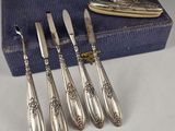 six antique silverware spoons and a knife on a blue cloth