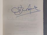 un livre ouvert, sur lequel figure une signature manuscrite, posé sur une table