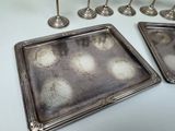 four silver trays on a white table with candles
