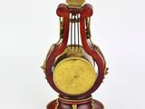 a red and gold clock on a stand on a white surface
