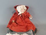 une vieille poupée vêtue d'une robe rouge et d'un bonnet, assise sur une table
